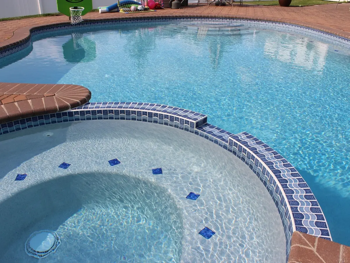 Piscina revestida en Diamond Brite color Cool Blue, con spa redondo y cenefa de mosaico azul