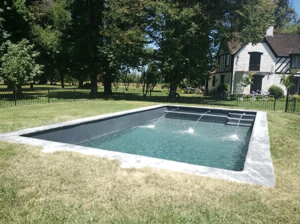 Piscina terminada con gel coat oscuro, llena y en funcionamiento, con la casa al fondo